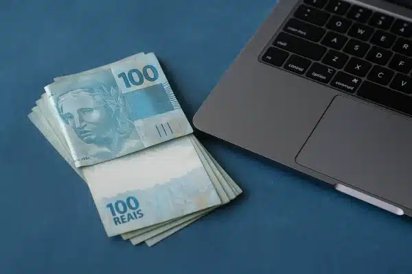 Renda Extra no Digital em 2026.Notas de 100 reais ao lado de um notebook representando trabalho digital e renda online