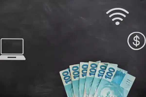 Notas de 100 reais ao lado de um notebook representando renda extra no digital em 2026