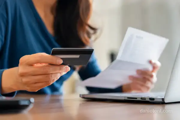 mulher segurando cartão de crédito e analisando contas no notebook em ambiente doméstico