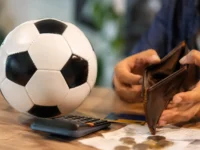 Copa do Mundo 2026 e dívidas: bola de futebol ao lado de carteira vazia, calculadora, cartão e recibos sobre a mesa