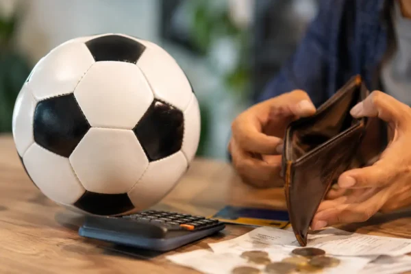 Copa do Mundo 2026 e dívidas: bola de futebol ao lado de carteira vazia, calculadora, cartão e recibos sobre a mesa