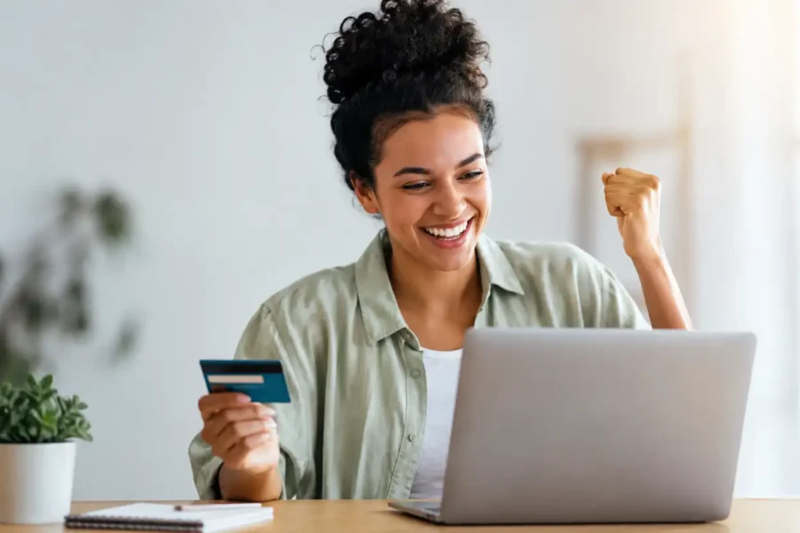 Empréstimo para MEI negativado com empreendedora segurando cartão bancário e comemorando em frente ao notebook.